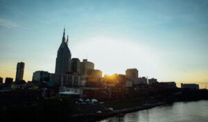 Sunset over the Nashville skyline with city buildings and the river in the foreground.