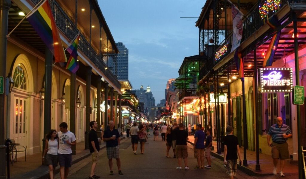 Evening view of Bourbon Street in New Orleans with colorful lights, balconies, and people walking.