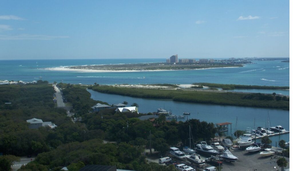 Aerial view of New Smyrna Beach, Florida, showing coastline, waterways, boats, and nearby high-rise buildings in the distance.