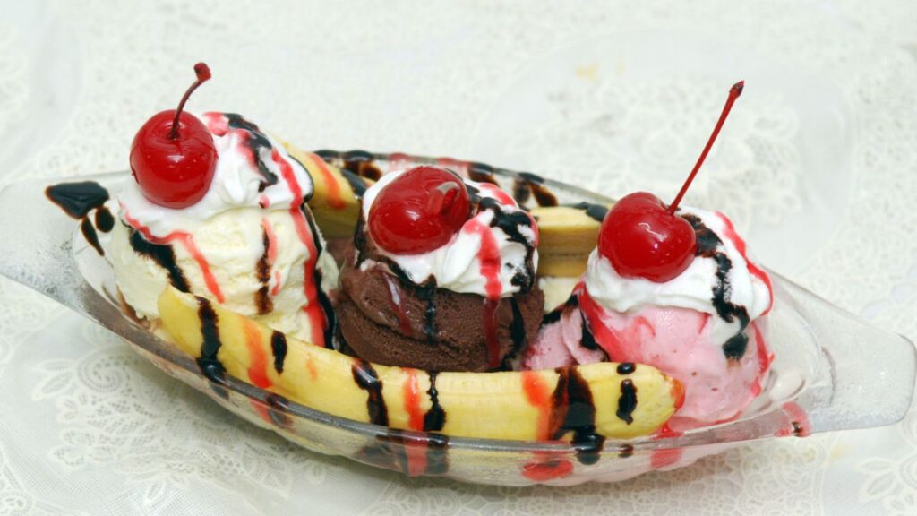 Banana split boat with vanilla, chocolate, strawberry scoops, whipped cream, chocolate drizzle, cherries.