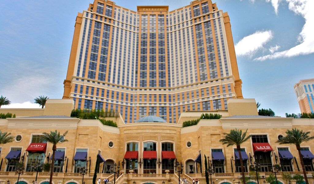 The Palazzo Hotel in Las Vegas, showcasing its towering structure with large windows and a grand entrance featuring shops and restaurants below.