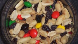 Close-up of a trail mix containing roasted peanuts, raisins, and colorful candy-coated chocolate pieces in a round container.