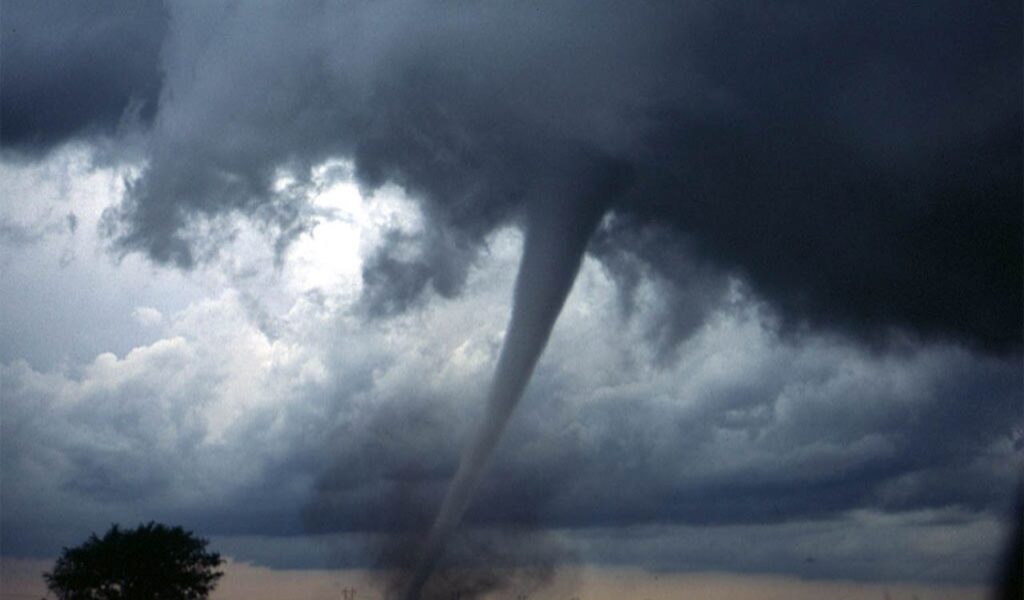 Dark storm clouds with a tornado touching down in an open field, emphasizing the importance of packing for extreme weather.