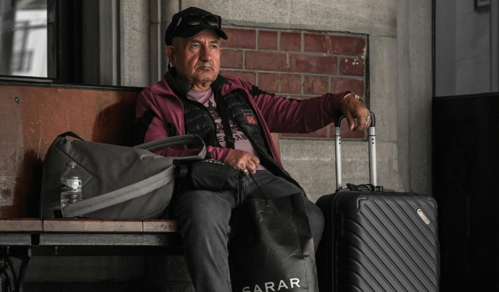 Senior traveler sitting at the airport with his luggage, looking relaxed while waiting for his flight.