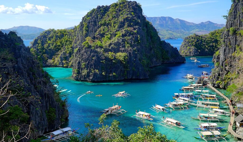 Traditional boats float on turquoise waters between limestone cliffs in Palawan, Philippines.