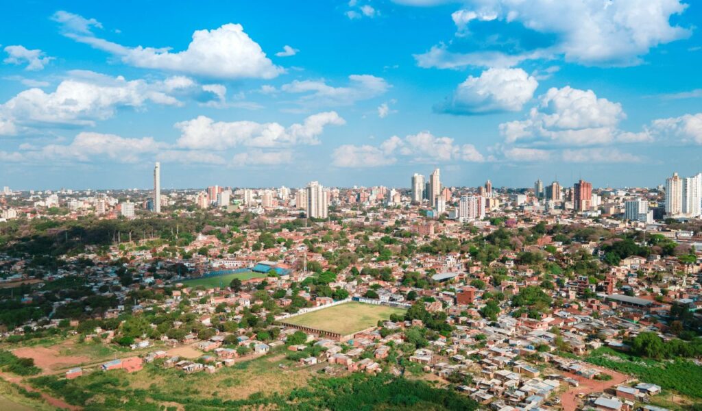 Aerial view of Asunción Paraguay showing a mix of urban buildings, residential areas, and green spaces under a blue sky with scattered clouds.