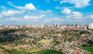Aerial view of Asunción Paraguay showing a mix of urban buildings, residential areas, and green spaces under a blue sky with scattered clouds.