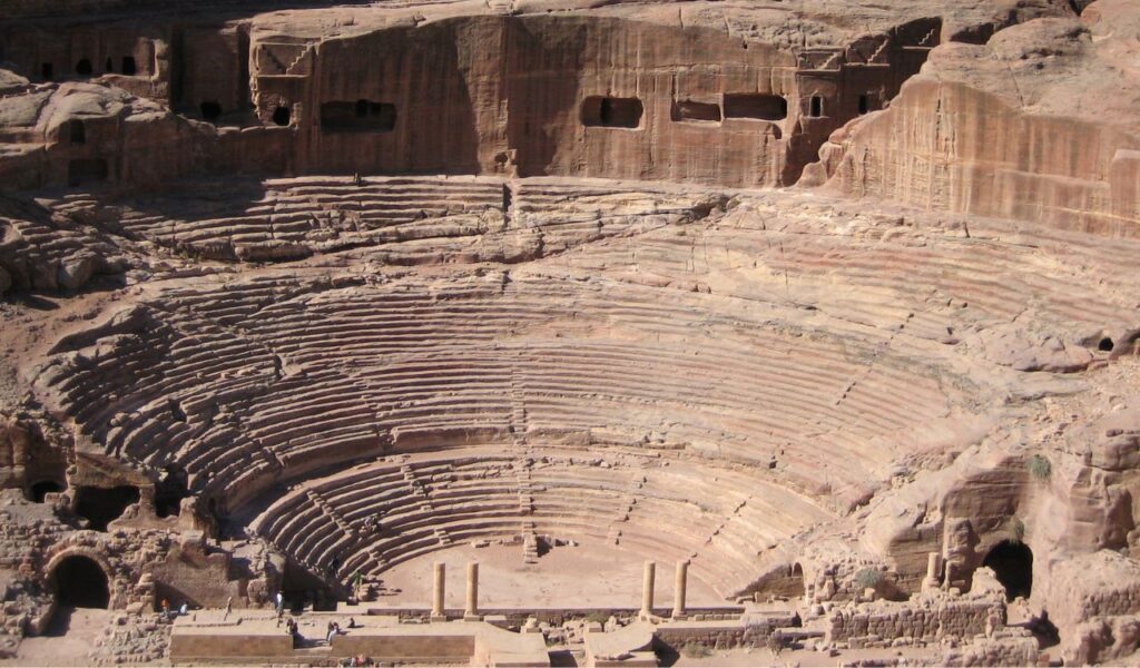 Ancient rock-carved amphitheater and cave dwellings in Petra, Jordan, showcasing Nabataean architecture and sandstone cliffs.