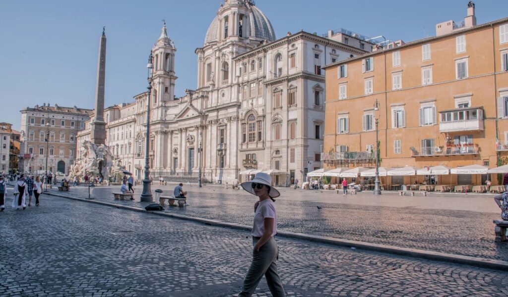 Piazza Navona in Rome with tourists walking, fountains, cafes, and the Baroque church of Sant'Agnese in Agone.