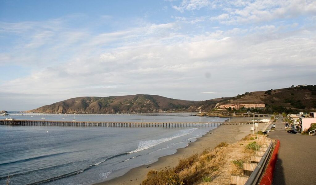 Calm shoreline and long pier at Pirate’s Cove near Avila Beach with hills in the background.