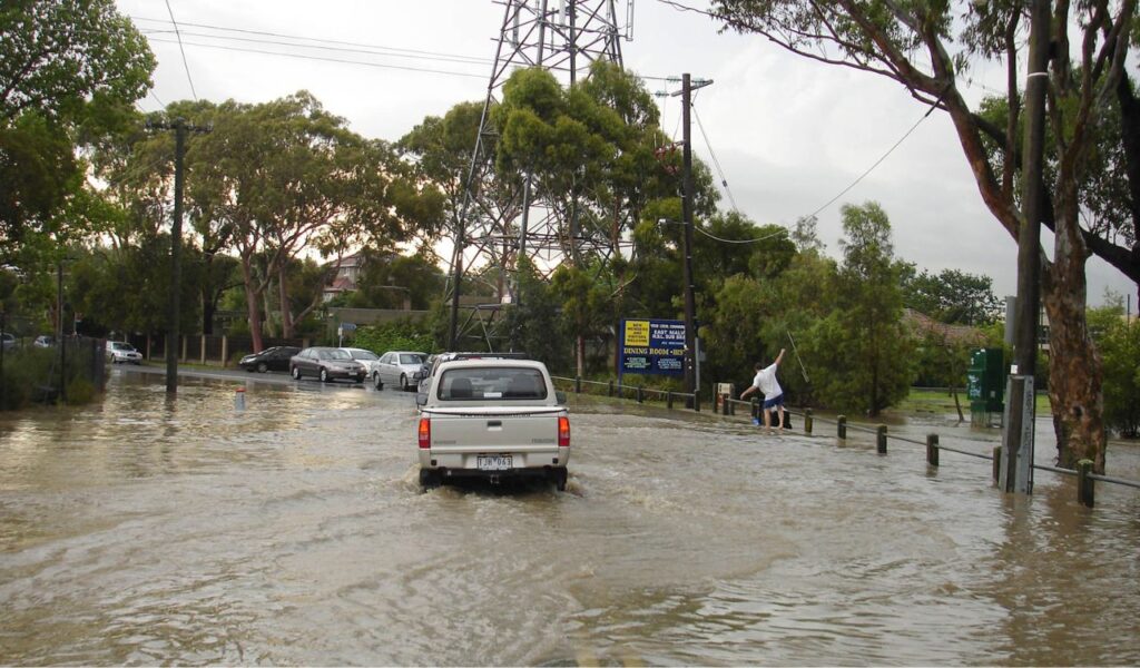 Vehicles driving through a heavily flooded urban street, highlighting the danger of flash flooding during severe weather.