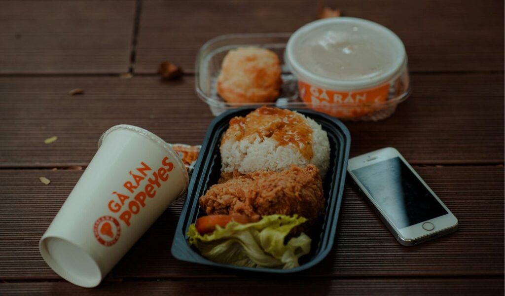 Popeyes Louisiana Kitchen meal featuring fried chicken, rice with gravy, a biscuit, and a drink, served on a wooden table with a smartphone beside it.