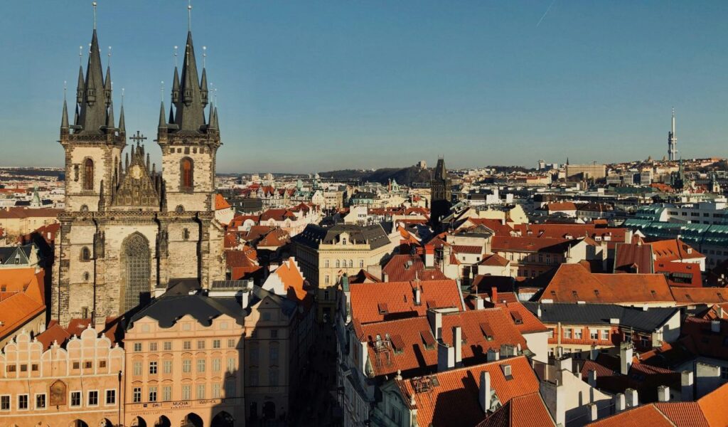 Scenic view of Prague’s Old Town with the Gothic Church of Our Lady before Týn rising above red-roofed buildings, under a clear blue sky.