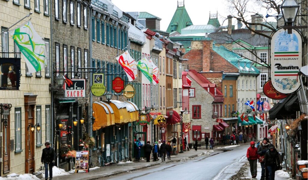 A charming street in Old Quebec lined with colorful buildings, flags, restaurants, and pedestrians enjoying a winter day.
