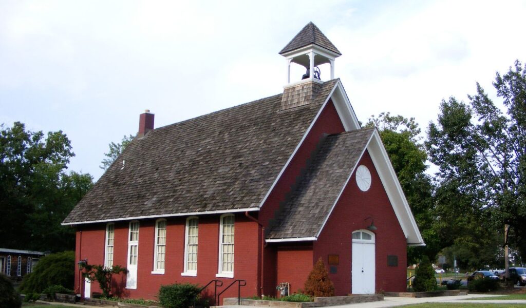 A bright red, one-room schoolhouse in Wisconsin with a shingled roof and bell tower, now converted into a cozy inn.