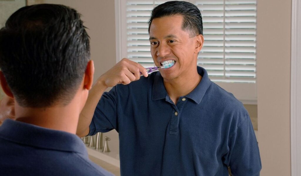 Man brushing his teeth in front of a mirror, practicing personal hygiene and freshening up after a long trip.