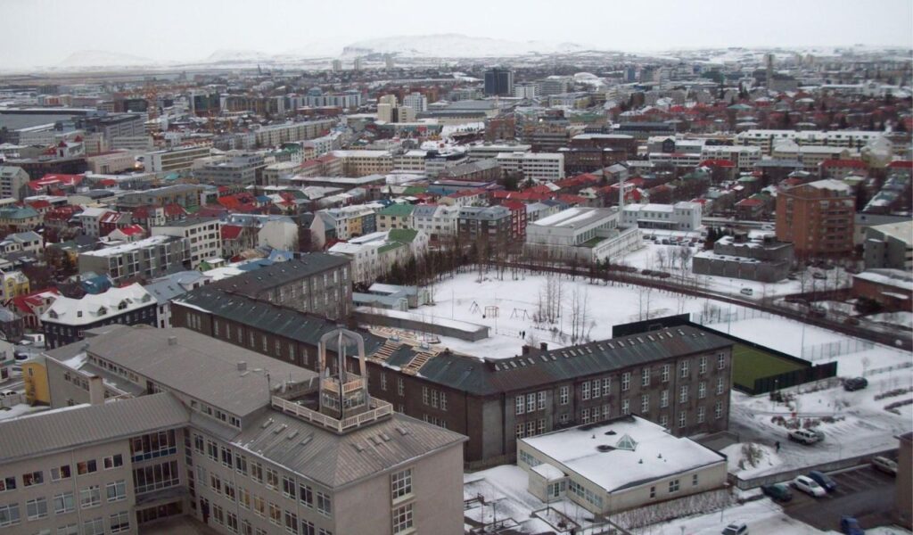 Aerial winter view of Reykjavík, Iceland with snow-covered buildings and distant mountain backdrop.