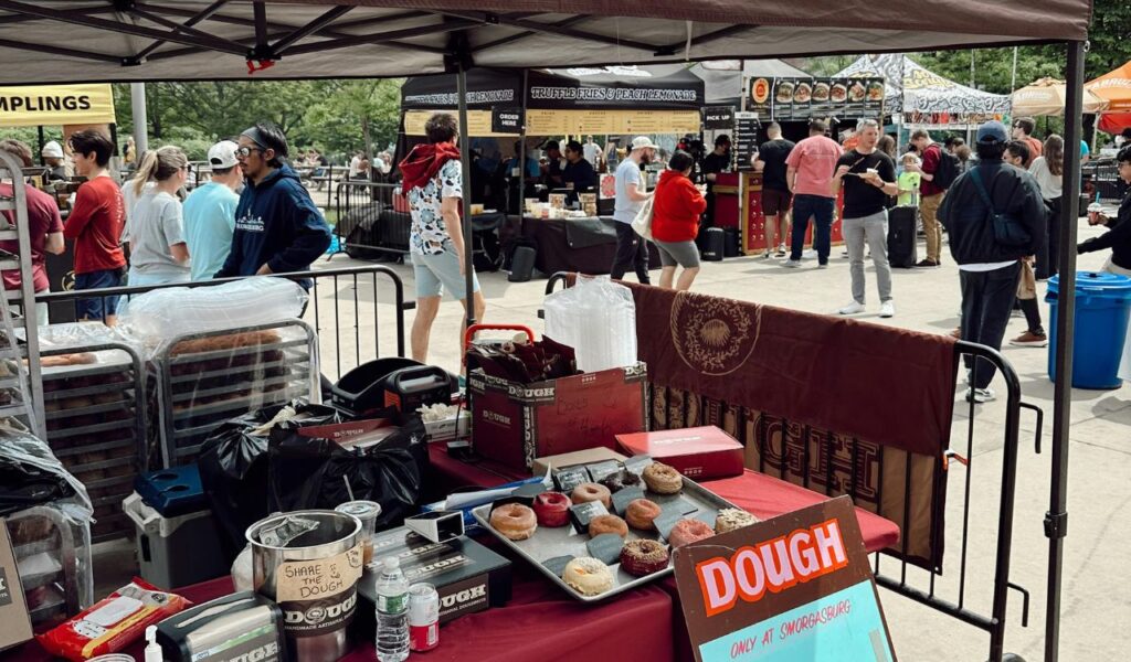 Artisan doughnut stall at an outdoor food market with people browsing various vendor booths in the background.