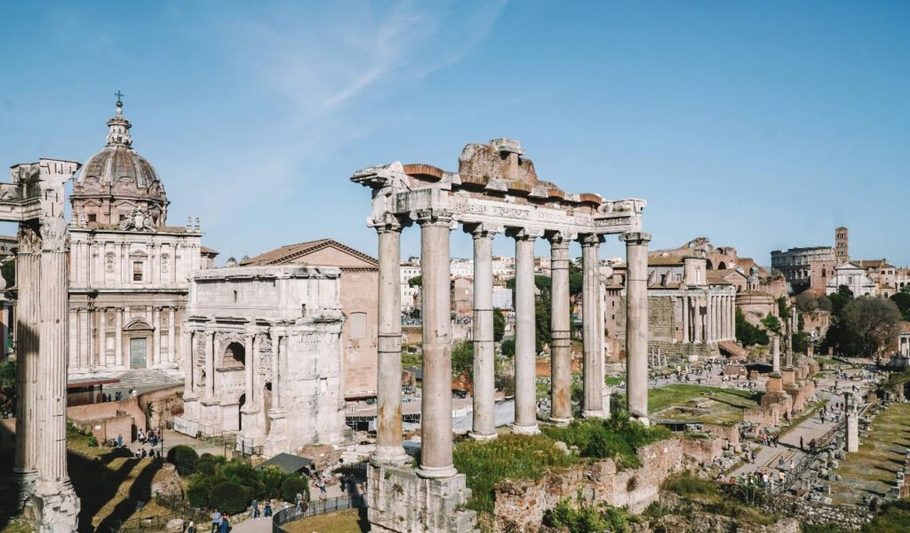 Ruins of the Roman Forum in Rome, Italy, featuring tall stone columns, ancient arches, and scattered relics.