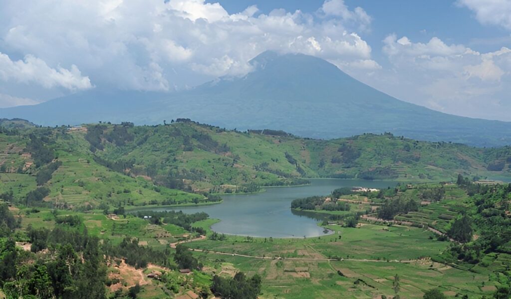 Lush green hills and a winding lake with a volcano in the background in rural Rwanda.
