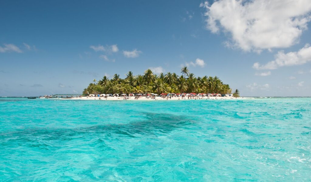 Remote tropical island with pristine clear waters and palm trees, showing a beach with tourists enjoying the sun.