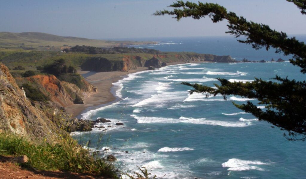 Waves rolling onto the sandy shore at San Carpoforo Creek Beach, with cliffs in the distance.