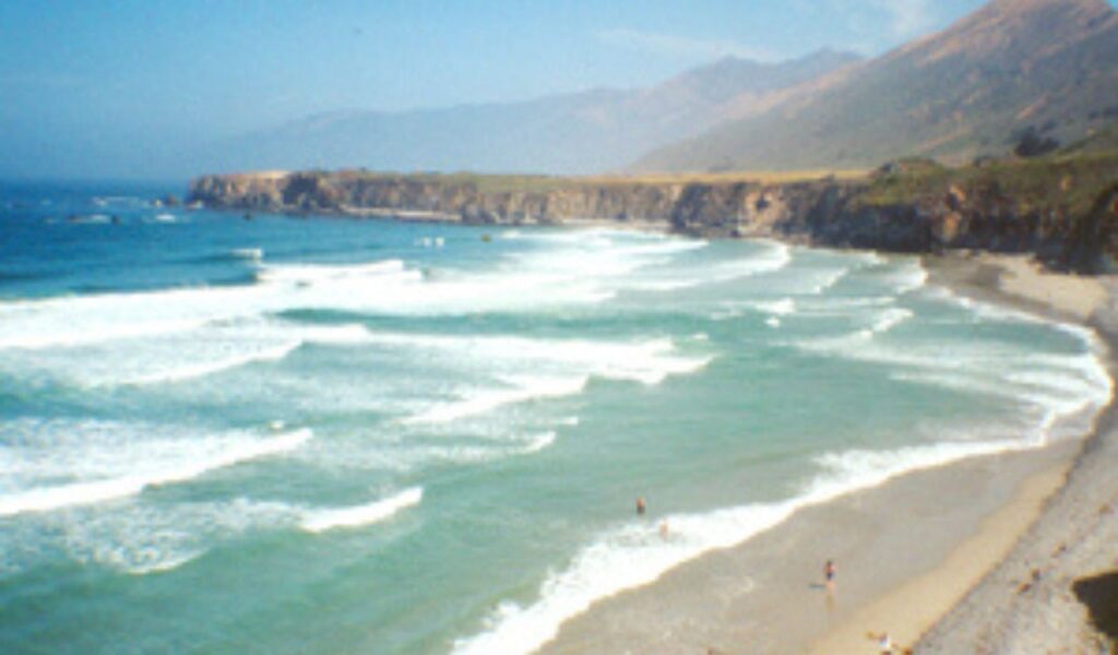 Waves crashing along the shore at Sand Dollar Beach in Big Sur with cliffs in the distance.