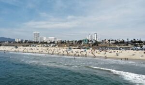 View of Santa Monica Beach with people on the sand, ocean waves, and city buildings in the background.