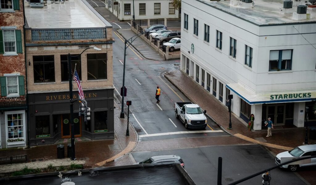 A rainy street view in Savannah, Georgia, featuring Rivers & Glen and Starbucks, with cars, pedestrians, and wet brick sidewalks.