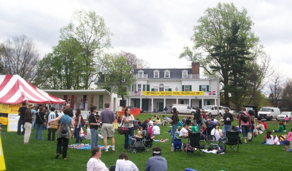 Families gathered on a lawn at the New Jersey Folk Festival, enjoying live music, food, and community on a spring day.