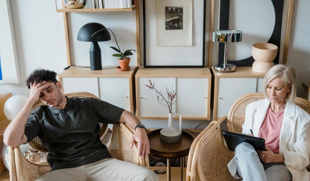 Frustrated man in a therapy session with a female therapist taking notes in a calm, modern office setting
