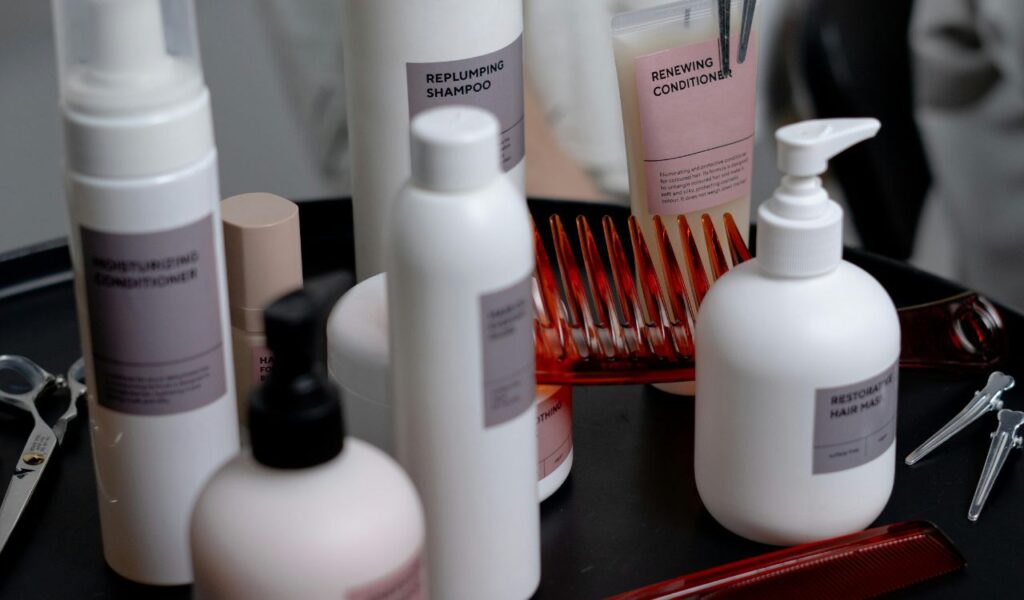  Hair care products including shampoo, conditioner, and hair masks arranged on a salon tray with combs, clips, and scissors.