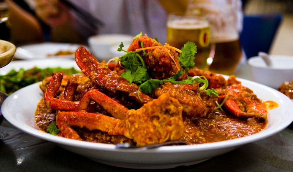 A plate of Singaporean chilli crab covered in rich, spicy red sauce, garnished with fresh herbs and served at a dining table.