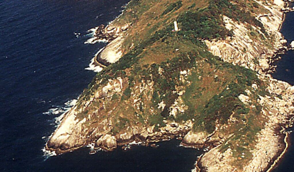 Aerial view of Snake Island with rocky cliffs, sparse greenery, and a lone lighthouse surrounded by the Atlantic Ocean.