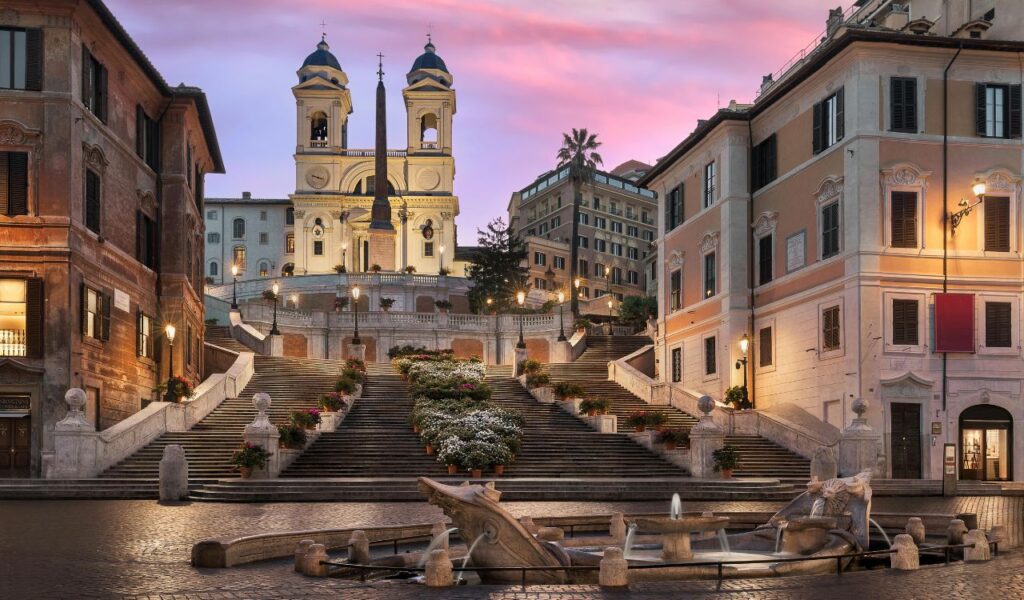 Spanish Steps in Rome at sunrise, with Trinità dei Monti church above, flower-lined stairs, and Fontana della Barcaccia.
