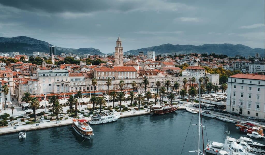 Historic Split waterfront with boats, palm trees, and Diocletian’s Palace tower framed by mountains in the background.