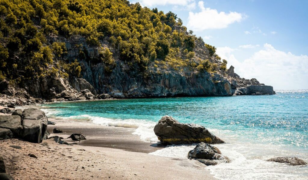 Secluded beach on St Barthelemy with turquoise waters, rocky cliffs, and golden sand under a bright sunny sky.