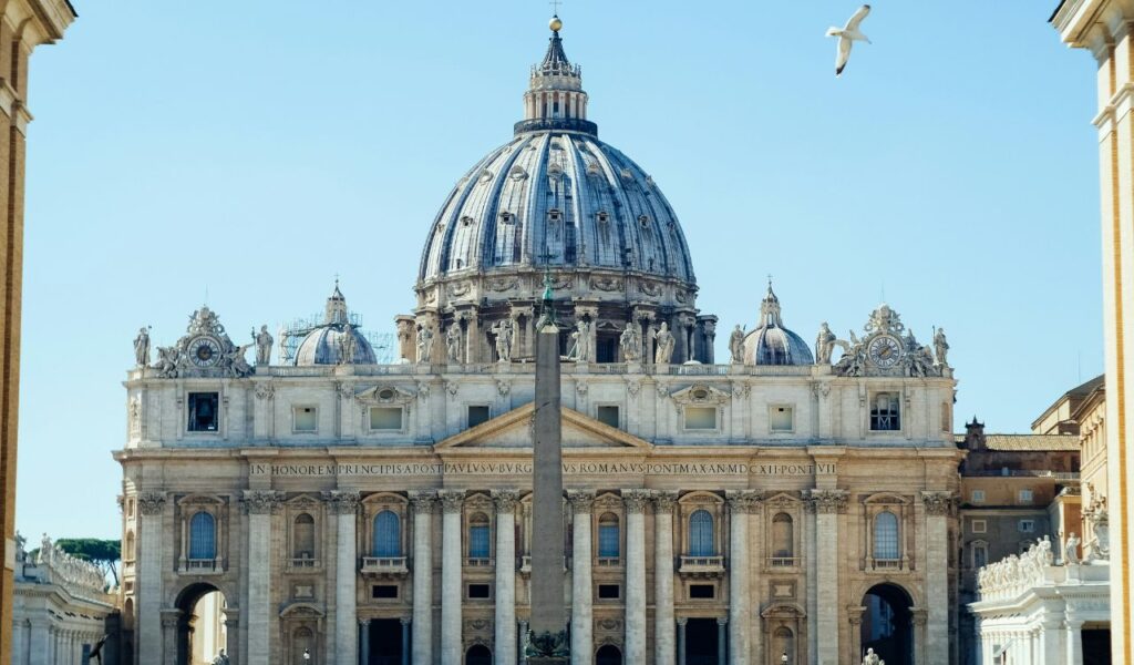 Front view of St Peter’s Basilica in Vatican City, with its grand dome, statues, columns, and a tall obelisk.