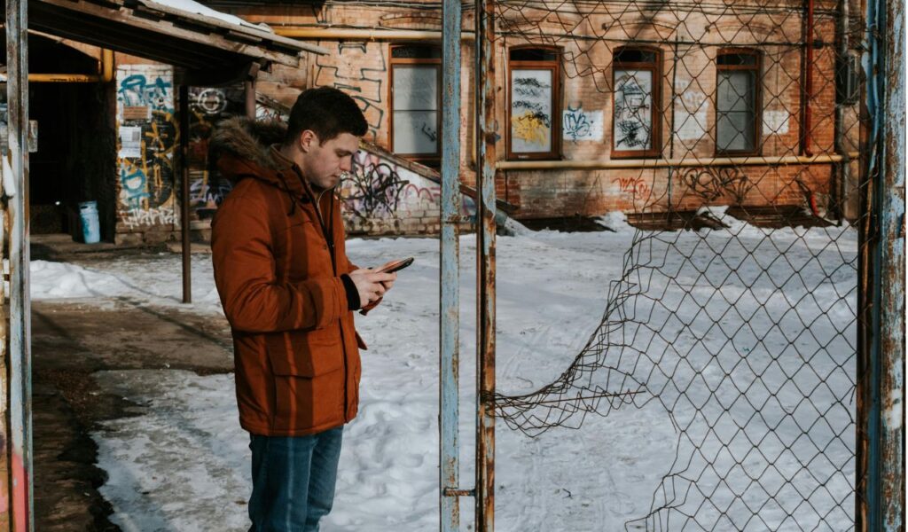 Man in a winter coat checking his phone in a snowy urban area, symbolizing staying informed about local weather updates.