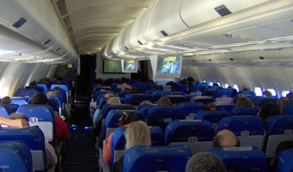 Economy class passengers seated with some stretching or moving, showing mid-flight comfort and light activity on board.