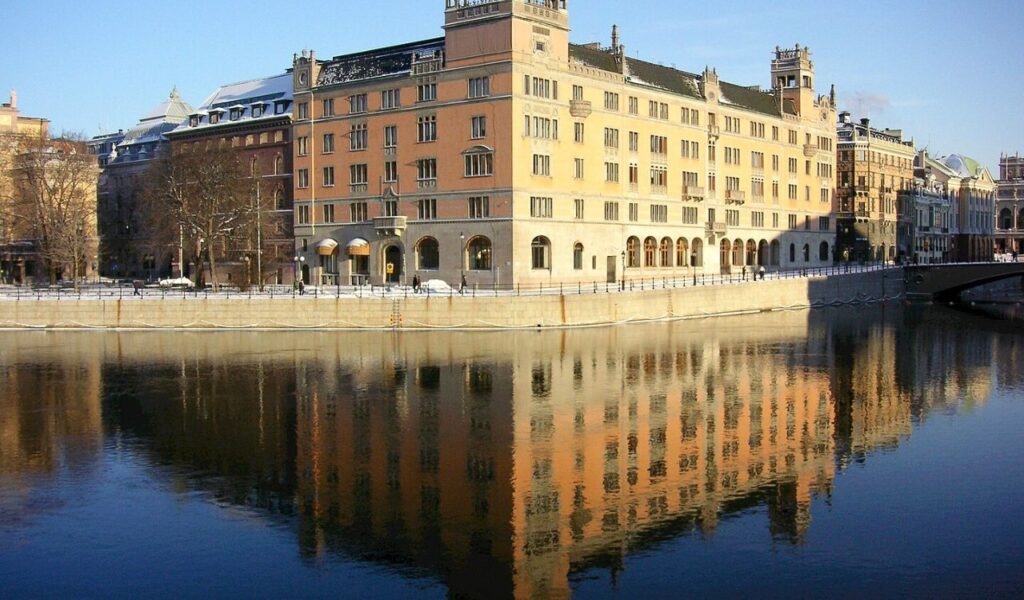 Rosenbad building in Stockholm, Sweden, reflecting in Norrström river on a clear winter day with historic charm.