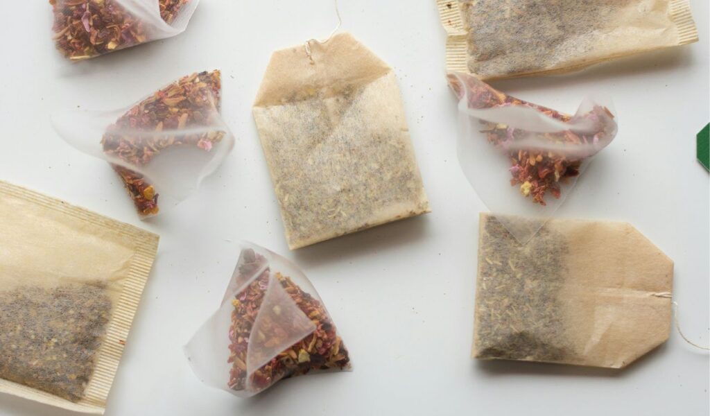  Assorted tea bags on a white surface, including traditional paper tea bags and pyramid-shaped mesh bags filled with loose herbal blends.