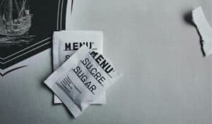 Close-up of white sugar packets labeled "Menu" placed on a table with part of a printed menu and torn wrapper visible.