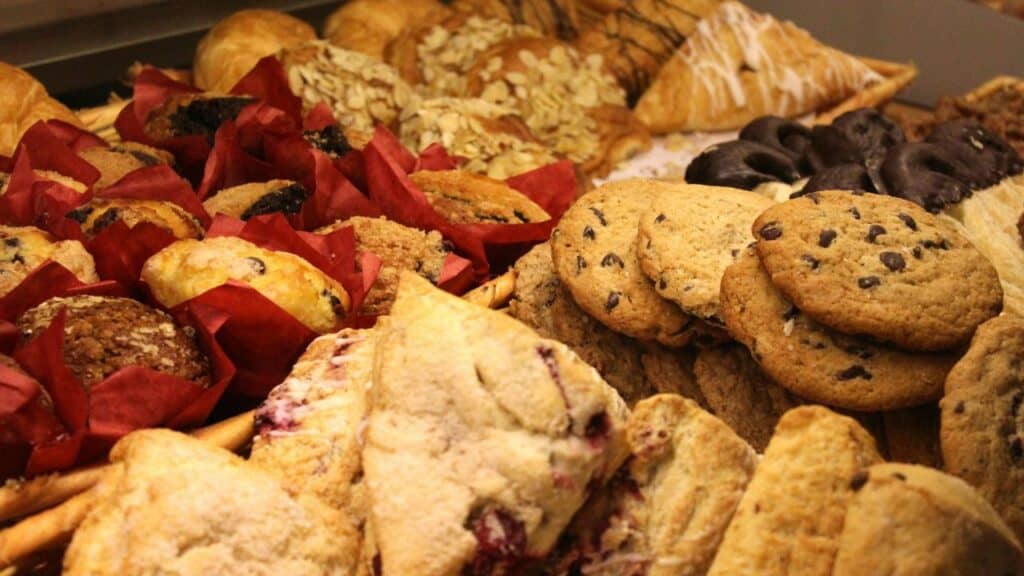 An assorted display of baked goods including chocolate chip cookies, muffins, scones, and pastries arranged in a bakery basket.