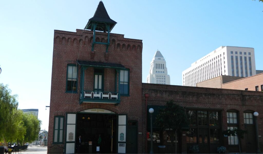Historic red-brick firehouse in Los Angeles, now transformed into The Firehouse Hotel with city skyscrapers in the background.