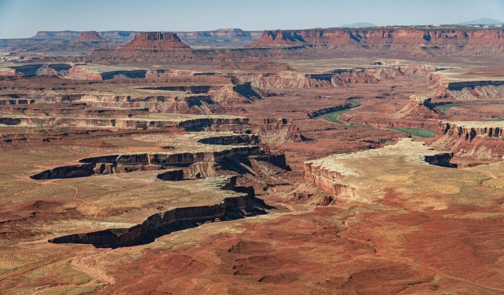 Aerial view of The Maze, Utah, with layered red canyons, cliffs, and a winding river cutting through the remote landscape.