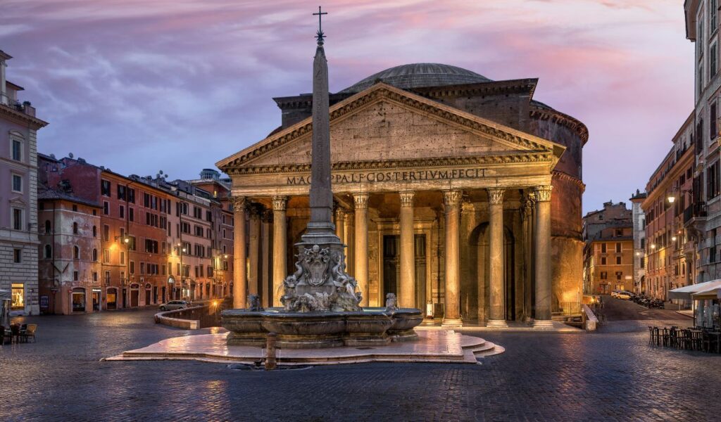 The Pantheon in Rome at dusk, with its grand columns, domed roof, and central fountain with an obelisk in front.