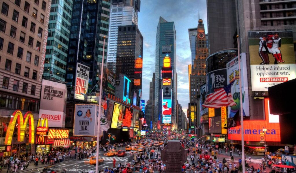 Times Square in New York City with bright billboards, crowds, and yellow taxis at dusk