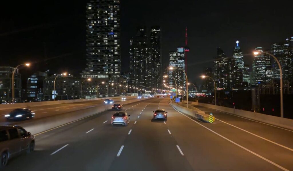 Cars driving on a well-lit city highway at night with visible headlights, highlighting safe low-light driving habits.