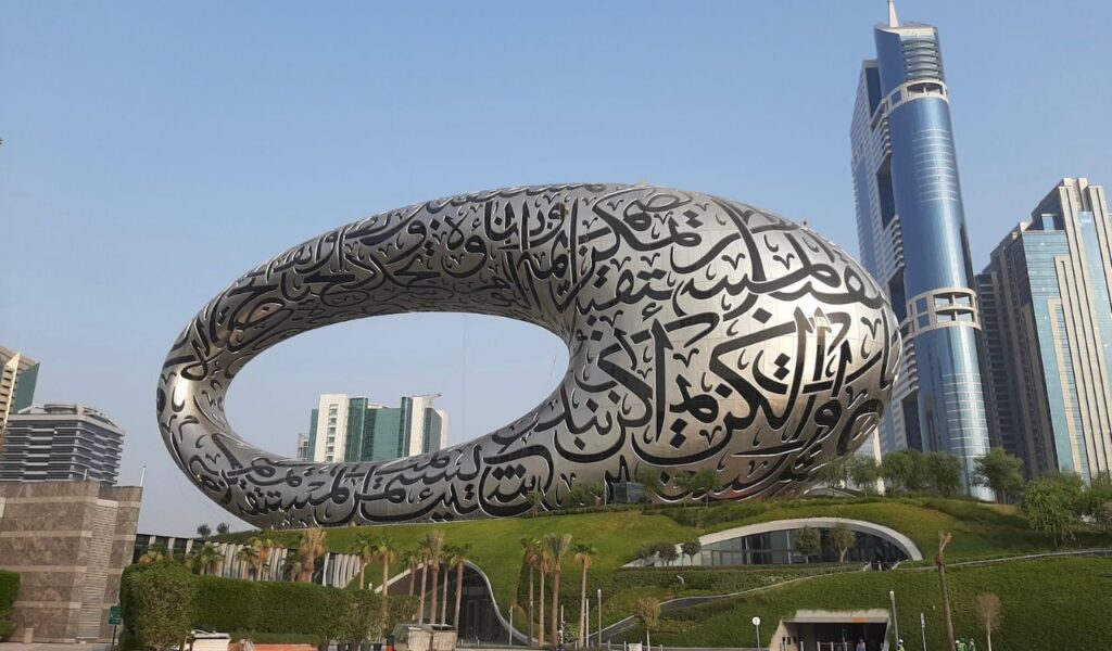 The Museum of the Future in Dubai, a futuristic torus-shaped building covered in Arabic calligraphy, stands prominently against a backdrop of modern skyscrapers.